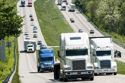 Multiple semi-trucks and vehicles on a divided highway representing the commercial transportation industry.
